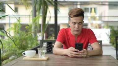 Mutlu Genç Asyalı adam açık havada kahve dükkanında telefon kullanma