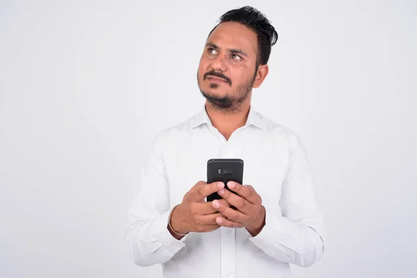 Estudio de toma de barbudo empresario indio usando el teléfono y pensando — Foto de Stock