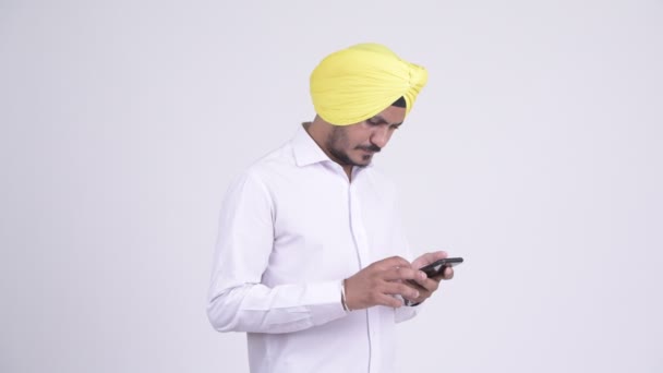 Barbudo indio Sikh hombre de negocios utilizando el teléfono y mirando sorprendido — Vídeo de stock