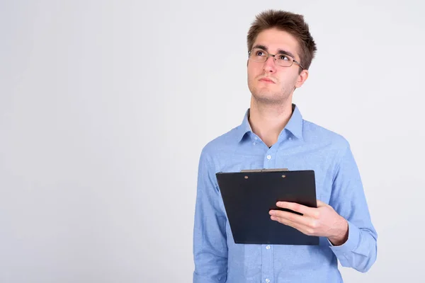 Young handsome businessman holding clipboard while thinking — Stock Photo, Image