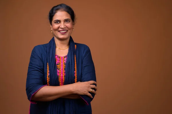 Happy mature Indian woman smiling against brown background — Stock Photo, Image