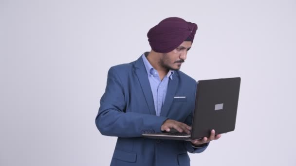 Boldog szakállas indiai szikh üzletember gondolkodás laptop használata közben — Stock videók