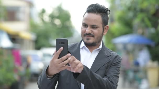 Glad skäggig indisk affärsman använder telefonen utomhus — Stockvideo