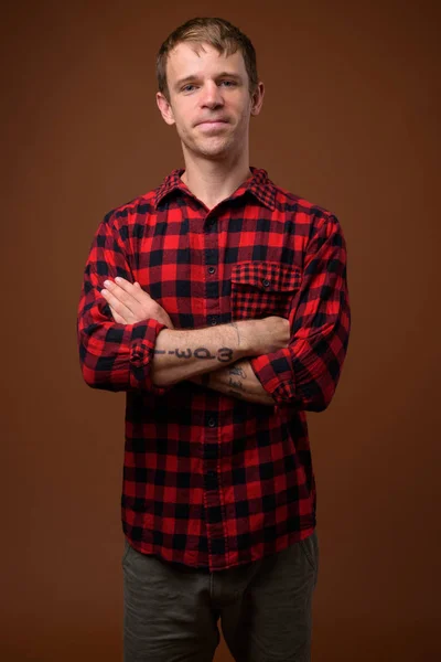 Hombre vistiendo camisa roja a cuadros contra fondo marrón —  Fotos de Stock