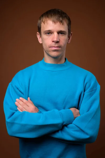 Man met blauwe trui tegen bruine achtergrond — Stockfoto