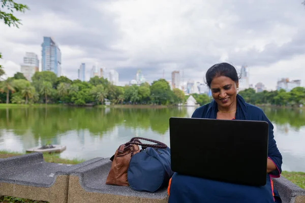 Портрет зрелой индийской женщины в парке с помощью ноутбука — стоковое фото