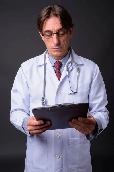 Mature handsome Italian man doctor thinking and holding clipboard — Stock Photo, Image