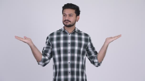 Porträt eines jungen glücklichen bärtigen indischen Mannes, der etwas vergleicht — Stockvideo