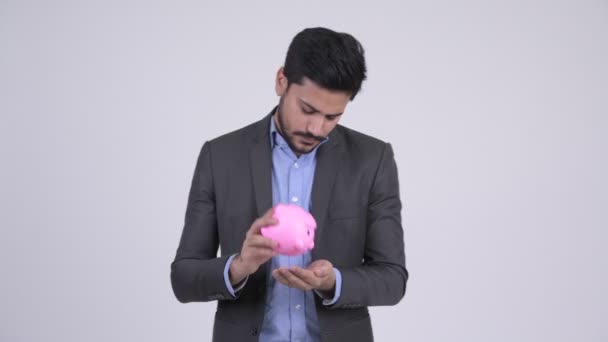 Jong gebaard Indiase zakenman bedrijf piggy bank en schouderophalend — Stockvideo