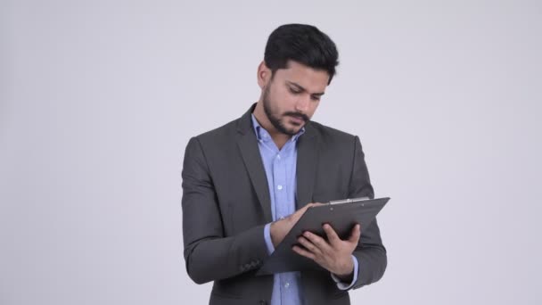 Молодой напряженный бородатый индийский бизнесмен показывает планшет и показывает большие пальцы вниз — стоковое видео