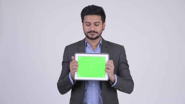 Young happy bearded Indian businessman thinking while showing digital tablet — Stock Video