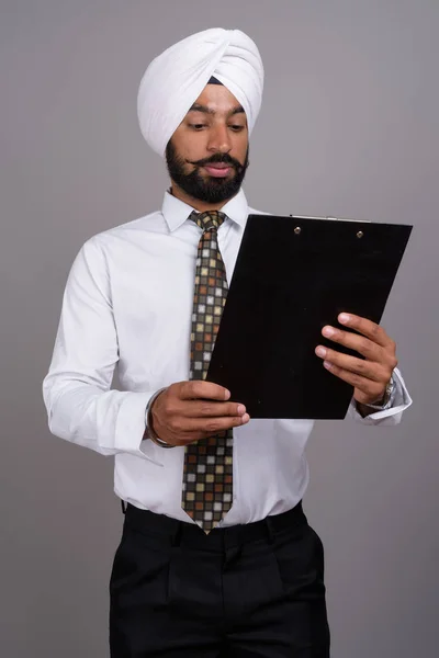 Young handsome Indian Sikh businessman wearing turban against gr