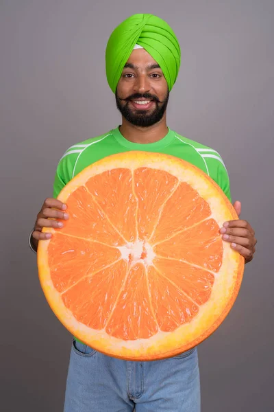 Joven hombre sikh indio guapo sosteniendo gran rebanada de naranja —  Fotos de Stock