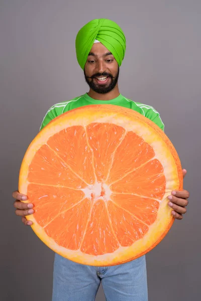 Joven hombre sikh indio guapo sosteniendo gran rebanada de naranja —  Fotos de Stock