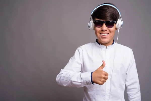 Junger asiatischer Teenager hört Musik vor grauem Hintergrund — Stockfoto