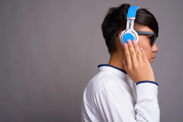 Junger asiatischer Teenager hört Musik vor grauem Hintergrund — Stockfoto