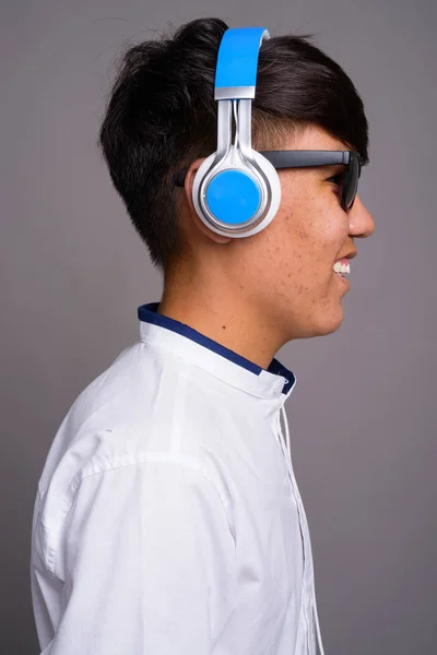 Stock image Young Asian teenage boy listening to music against gray backgrou