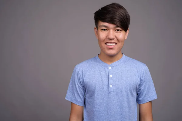 Mladý asijské dospívající chlapec proti šedé pozadí — Stock fotografie