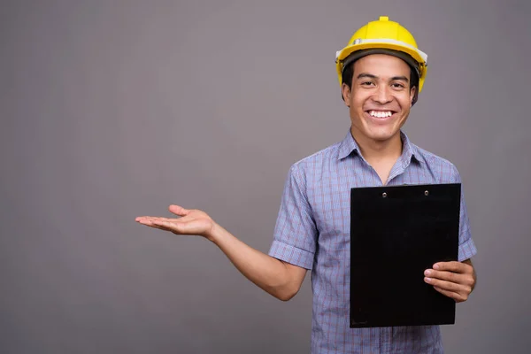 Young Asian businessman wearing hardhat against gray background — Stock Photo, Image