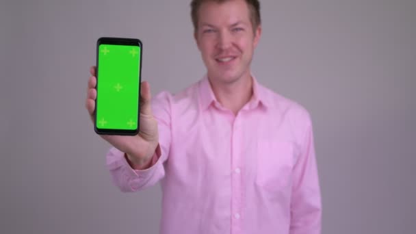 Щасливий молодий красивий бізнесмен показує телефон і дає великі пальці вгору — стокове відео