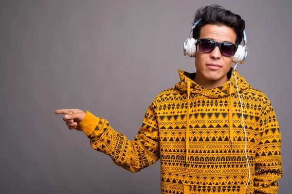 灰色の背景の下で音楽を聴く若いアジア人男性 — ストック写真