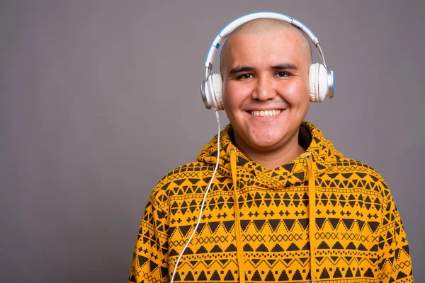 Junger Asiate mit Glatze hört Musik vor grauem Hintergrund — Stockfoto
