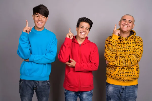 Tres hombres asiáticos jóvenes usando ropa de abrigo contra el backgro gris —  Fotos de Stock