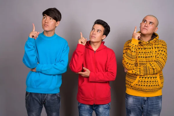Trzech młodych mężczyzn Azjatki sobie ciepłe ubranie przed szary backgro — Zdjęcie stockowe