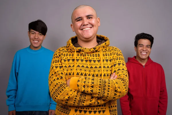 Drei junge asiatische Männer in warmer Kleidung vor grauem Backgro — Stockfoto