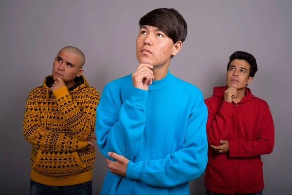 Üç Genç Asyalı adam gri backgro karşı sıcak giysiler giyiyor — Stok fotoğraf