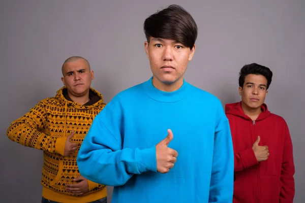 Három fiatal ázsiai férfiak szürke backgro ellen meleg ruházat viselése — Stock Fotó