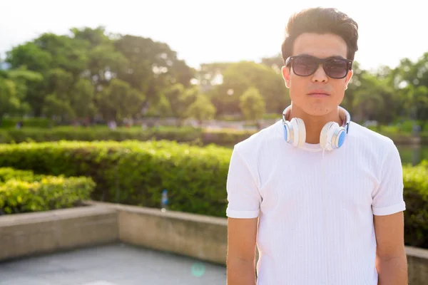 Молодий азіатський чоловік у навушниках під час відпочинку в парку. — стокове фото