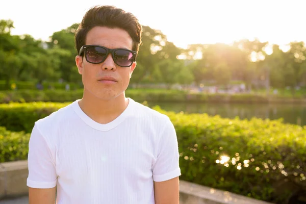 Joven asiático hombre usando gafas de sol mientras se relaja en el parque —  Fotos de Stock