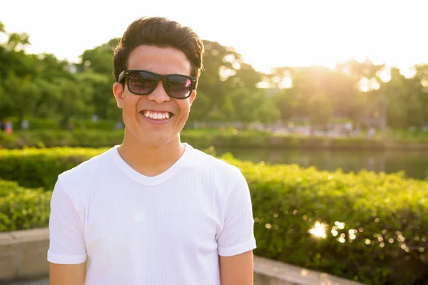 Joven asiático hombre usando gafas de sol mientras se relaja en el parque —  Fotos de Stock