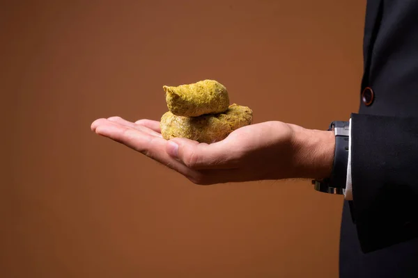 Hand eines jungen Geschäftsmannes hält Poop vor braunem Hintergrund — Stockfoto