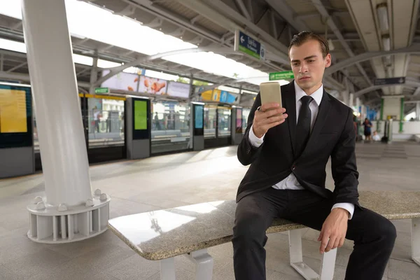 Young businessman using mobile phone at train station — Stock Photo, Image