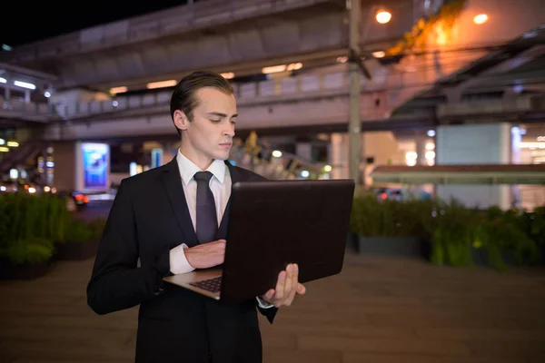 Zakenman met laptopcomputer buiten 's nachts in de stad — Stockfoto