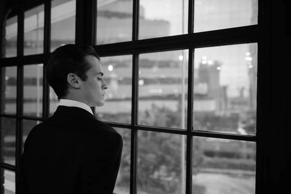 En ung forretningsmann som ser ut av vinduet og tenker: – stockfoto