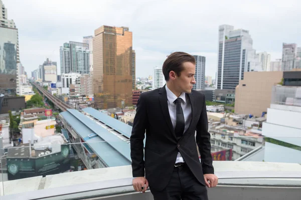 Young businessman thinking outdoors in city with rooftop view — Stock Photo, Image