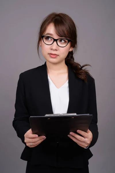 Young beautiful Asian businesswoman against gray background — Stock Photo, Image