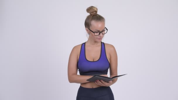 Glückliche junge schöne blonde Frau liest Buch mit Brille — Stockvideo