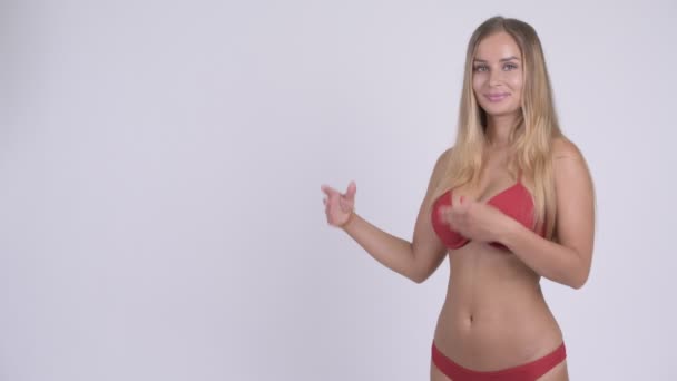 Glückliche junge schöne blonde Frau im Bikini zeigt etwas — Stockvideo