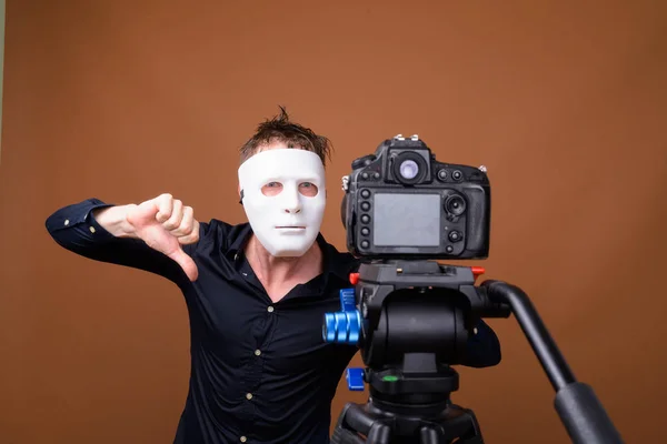 Young man wearing mask while vlogging and showing thumb down