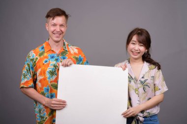 Gülümseyen ve boş beyaz tahta tutan bir çok etnik turist çift