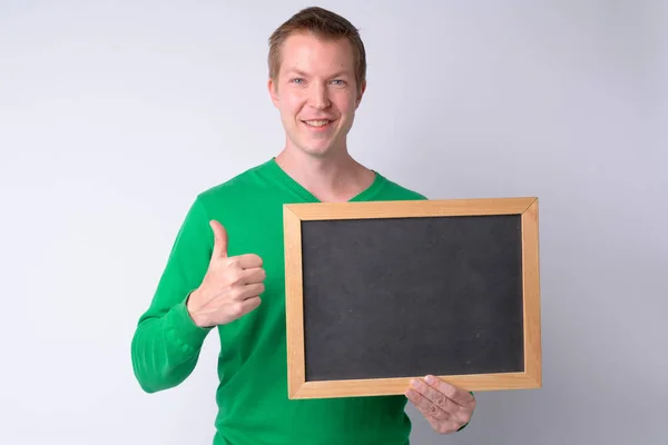 Happy young handsome man holding blackboard and giving thumbs up — Stock Photo, Image