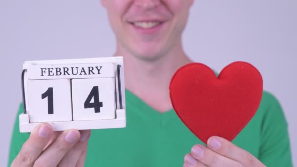Happy young handsome man with calendar block and heart — Stock Video