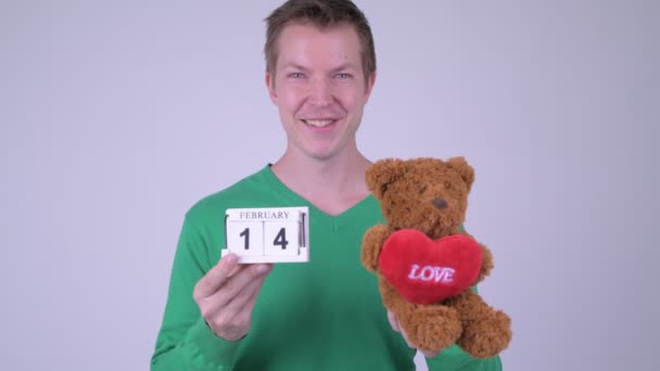 Happy young handsome man with calendar block and teddy bear — Stock Video