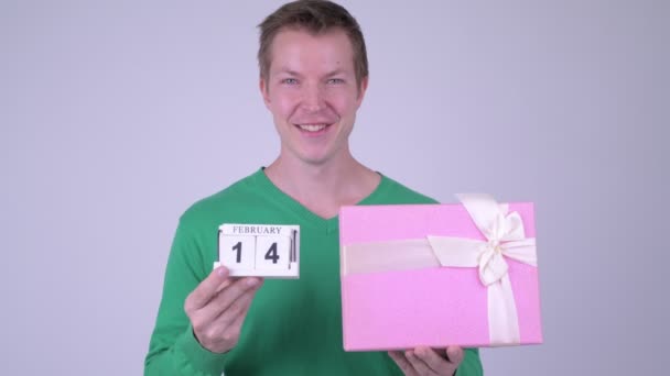 Счастливый молодой красивый мужчина с блоком календаря и подарочной коробкой — стоковое видео