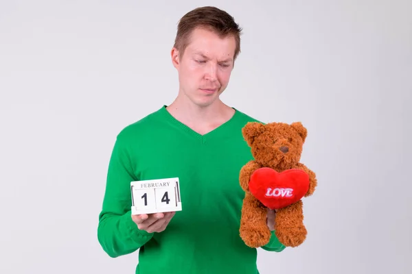 Sad young man holding calendar block and teddy bear for Valentines day — Stock Photo, Image