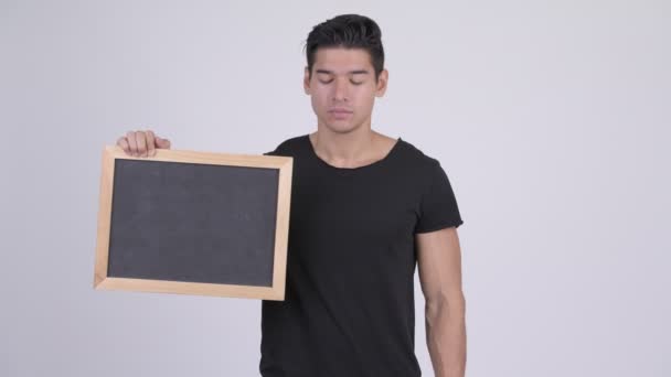 Jovem estressado multi-étnico homem segurando quadro negro e dando polegares para baixo — Vídeo de Stock